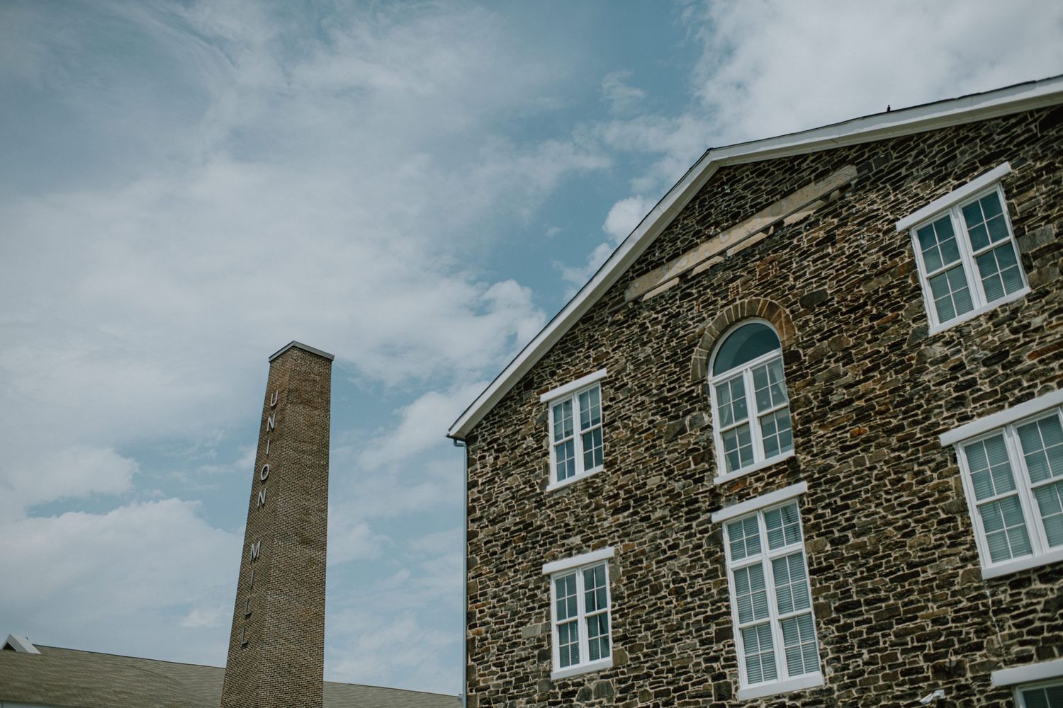Historic stone building with white windows and tall chimney against blue sky.