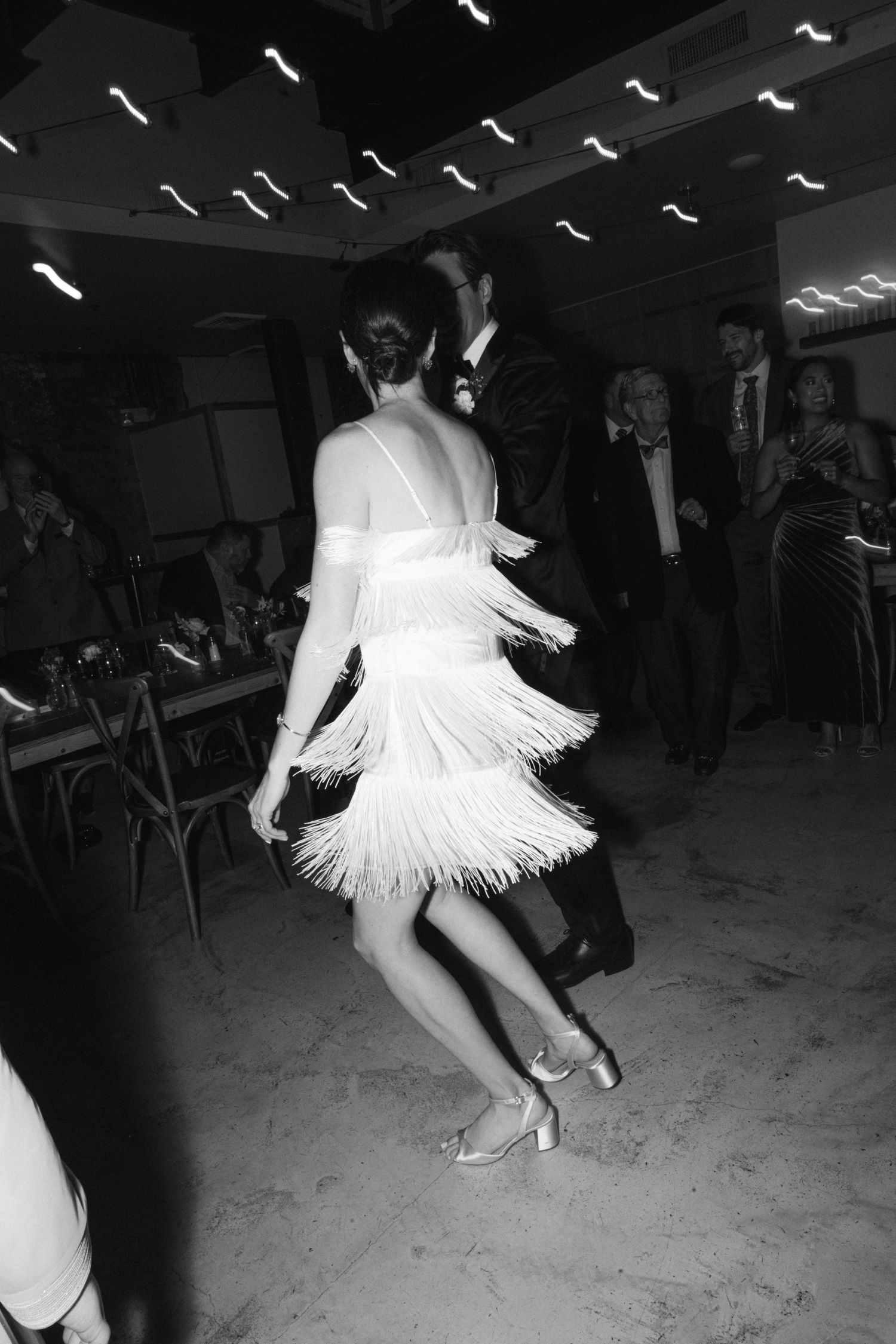 A dynamic dance scene showing a white fringe dress twirling under modern ceiling lights.