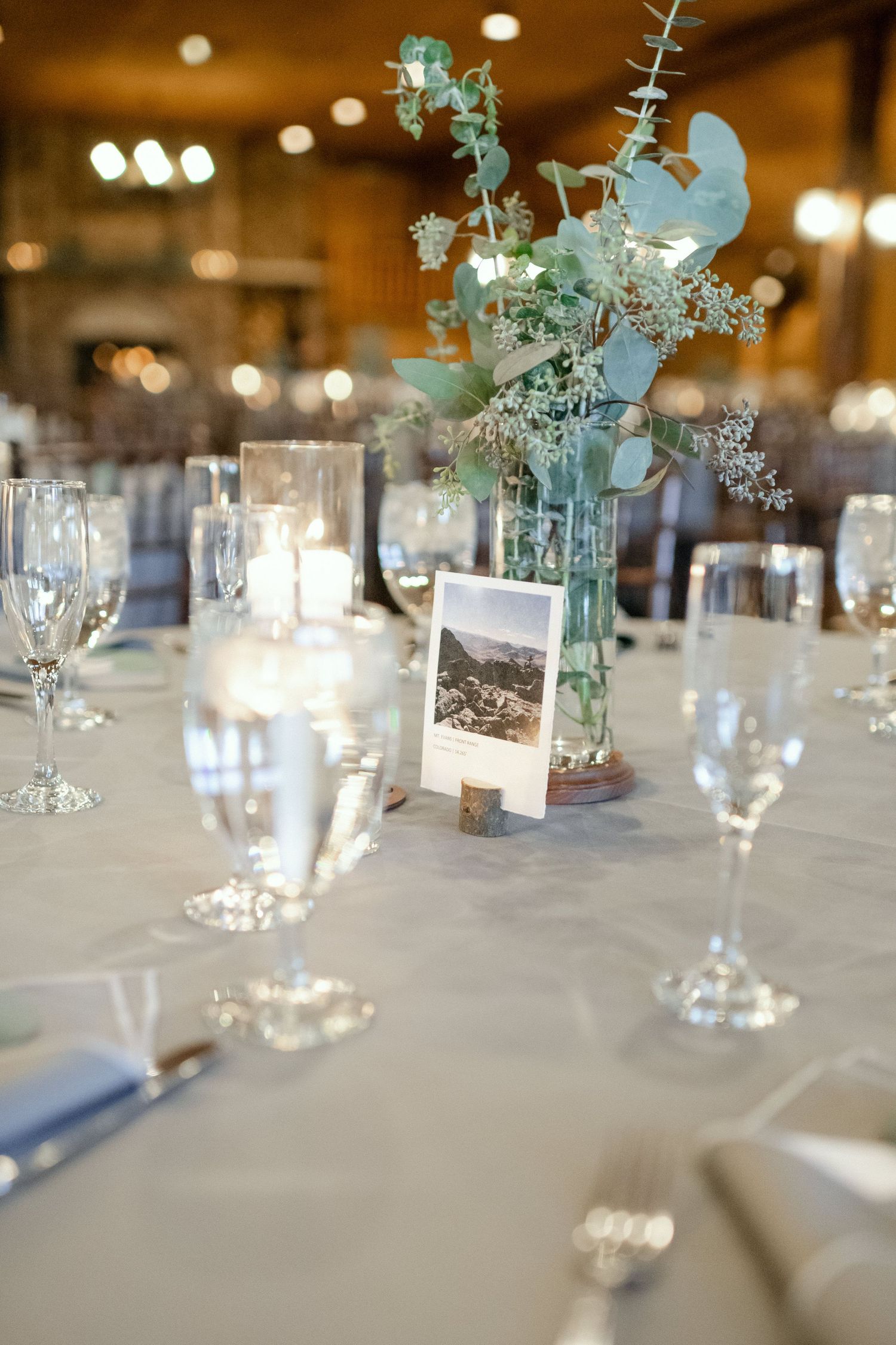 Elegant wedding table setting with eucalyptus centerpiece, wine glasses, and photo card decor.