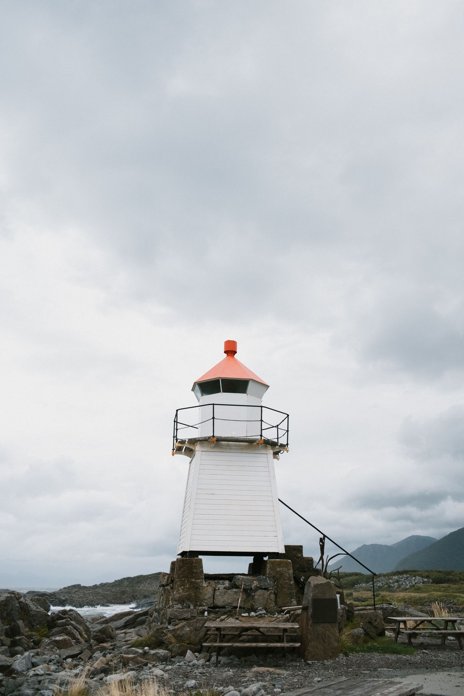 Small white lighthouse with red top stands on rocky coastal outcrop under cloudy skies.