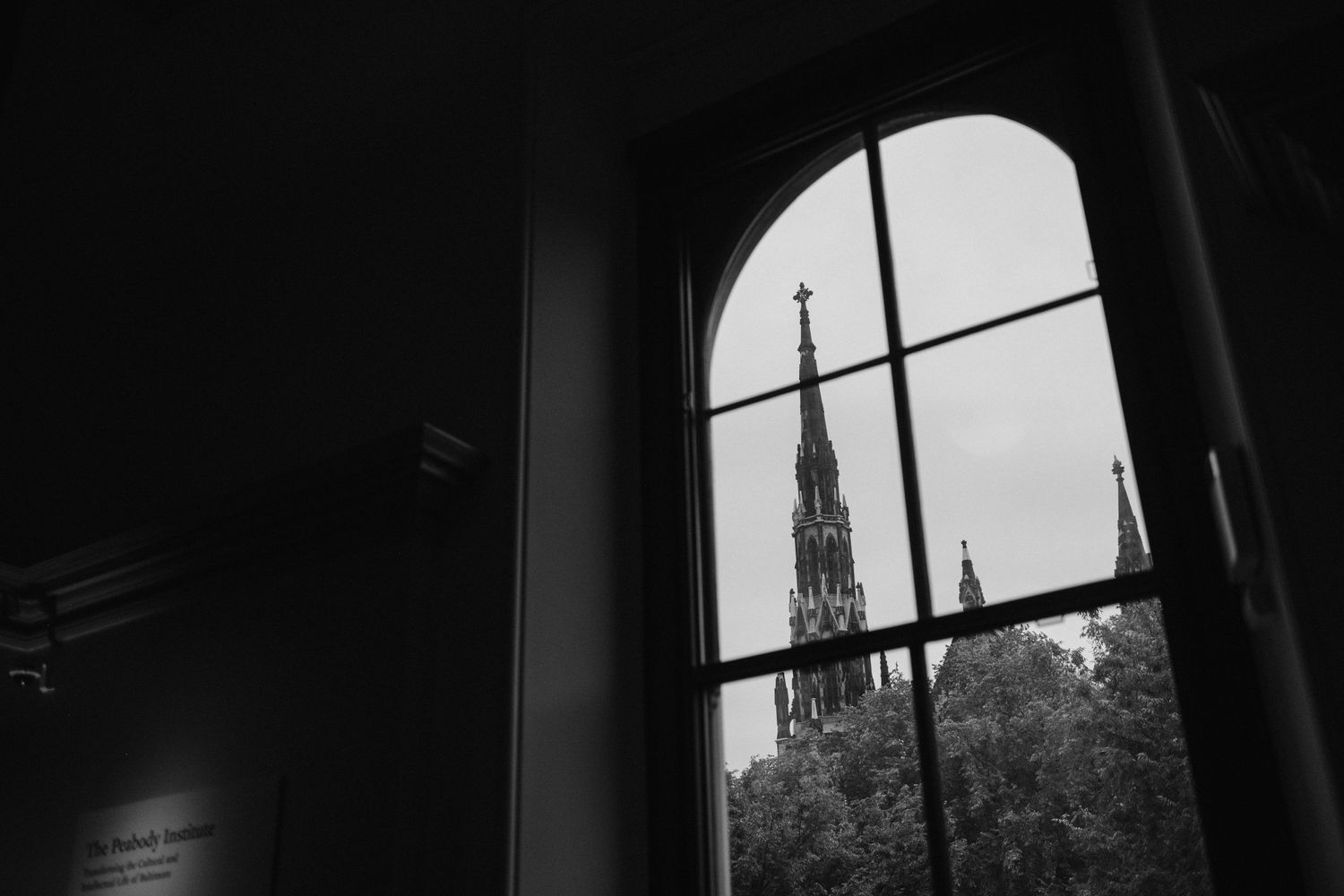 Black and white view of a church spire through an arched window.