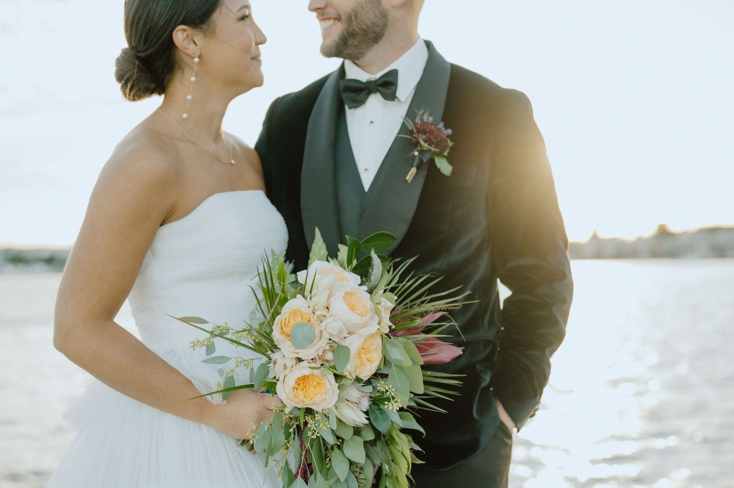 Elegant wedding portrait on a dock with bride holding a peach and green floral bouquet.