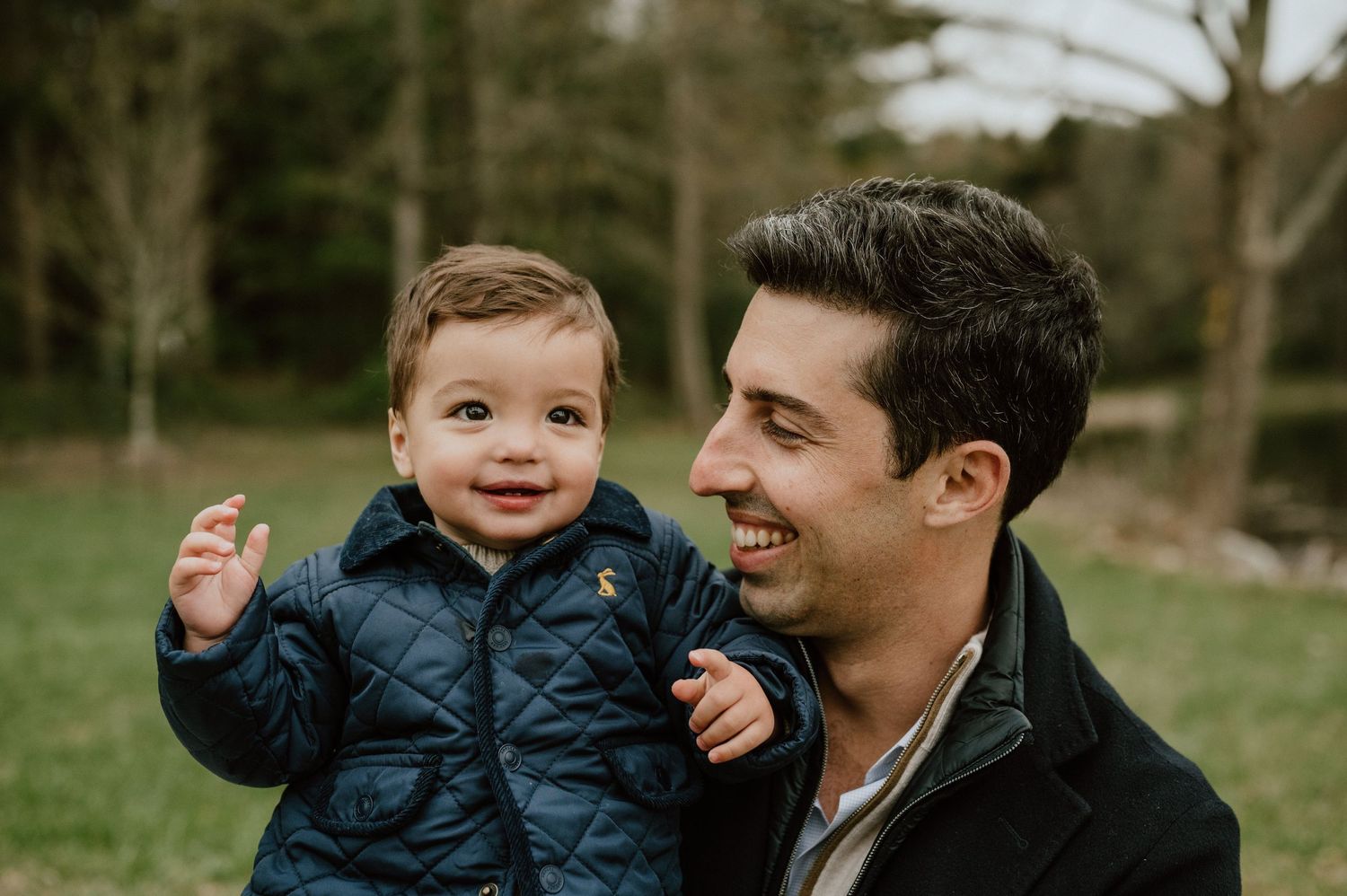 A heartwarming outdoor portrait of a toddler in a navy puffer jacket being held while laughing.