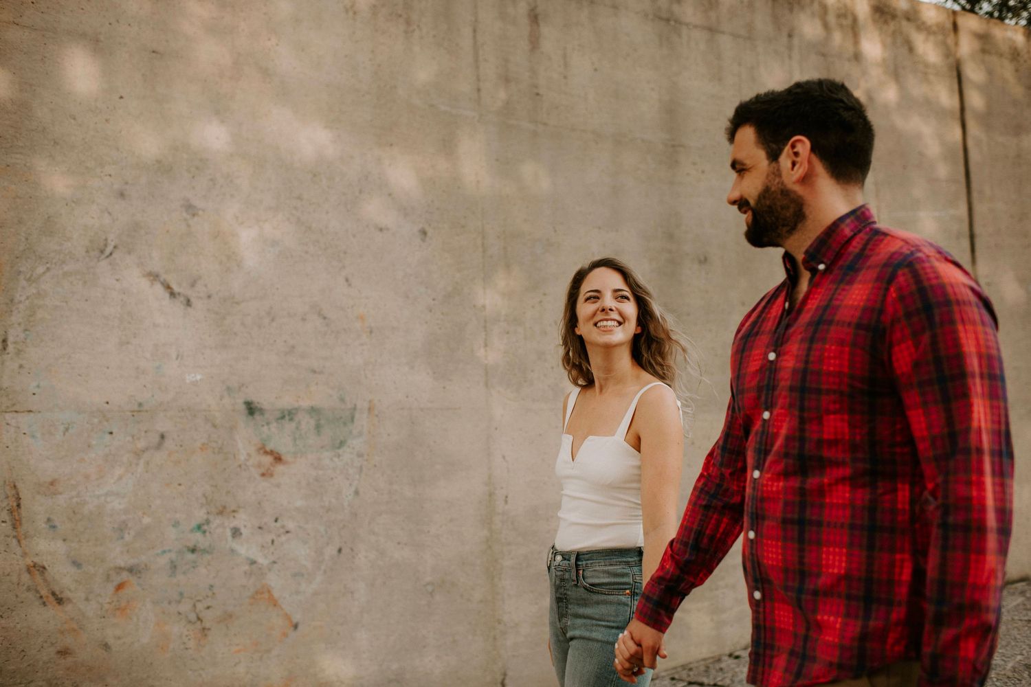 Couple sharing joyful moment against textured wall in urban setting.