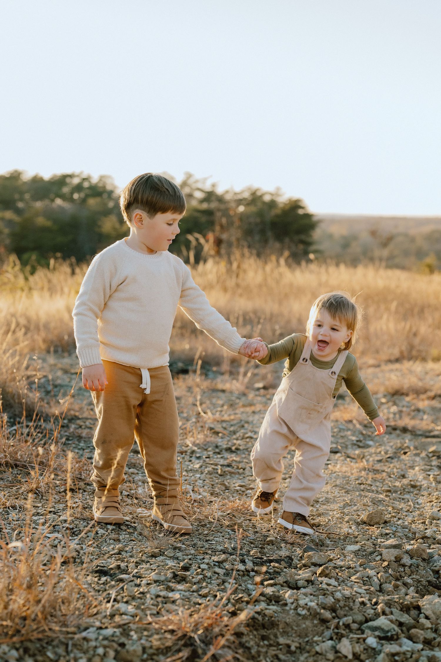 Two children hold hands while playing in a sun-lit field.
