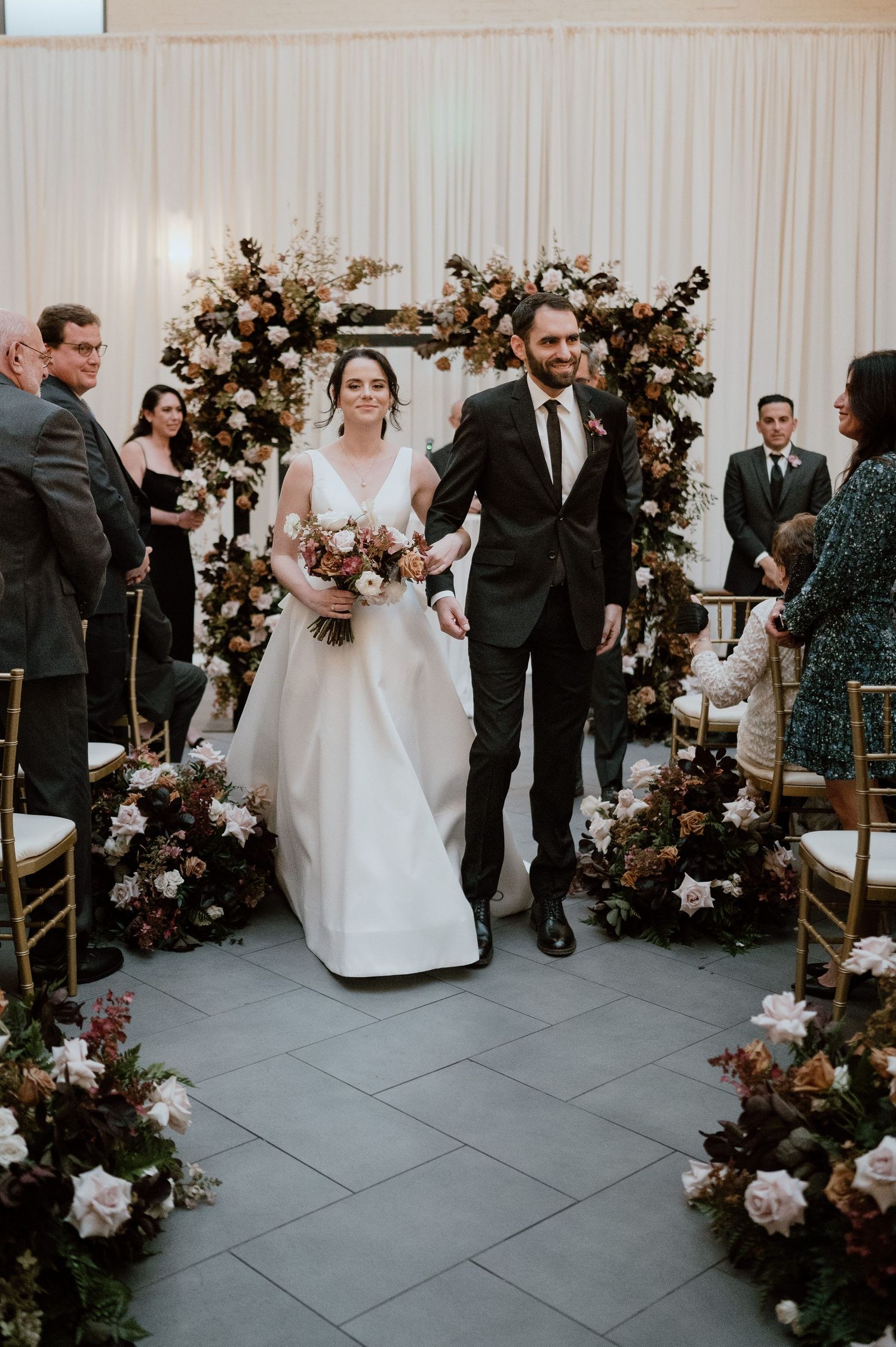 Wedding recessional through floral arch with guests seated on either side.