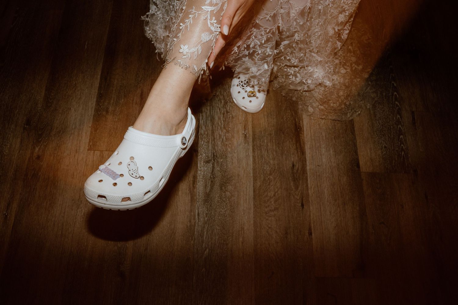White Crocs shoes on hardwood floor with party lighting.