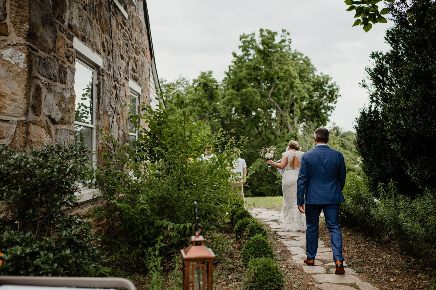 A couple walking along a stone path beside a historic building with lush landscaping.