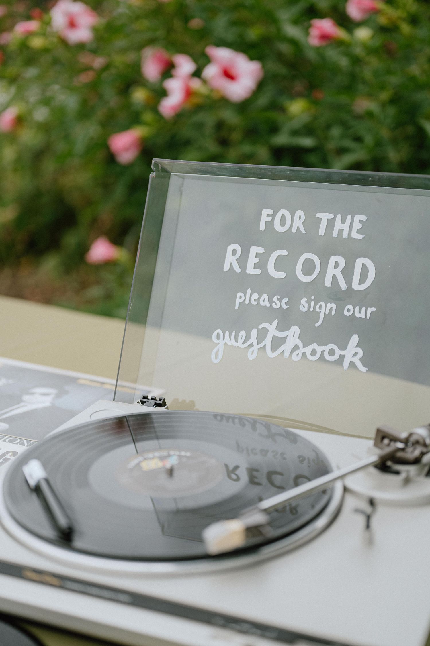 A vintage record player displaying a sign that reads 'For the record please sign our guestbook' with pink flowers.