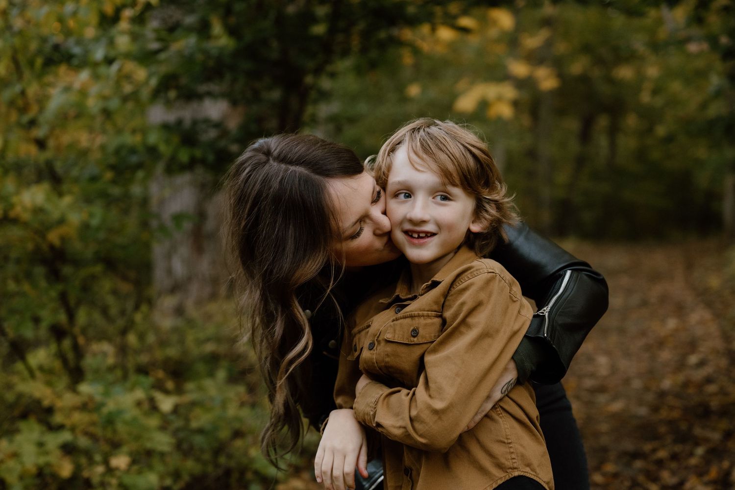 A sweet moment of affection captured outdoors with fall colors in the background.