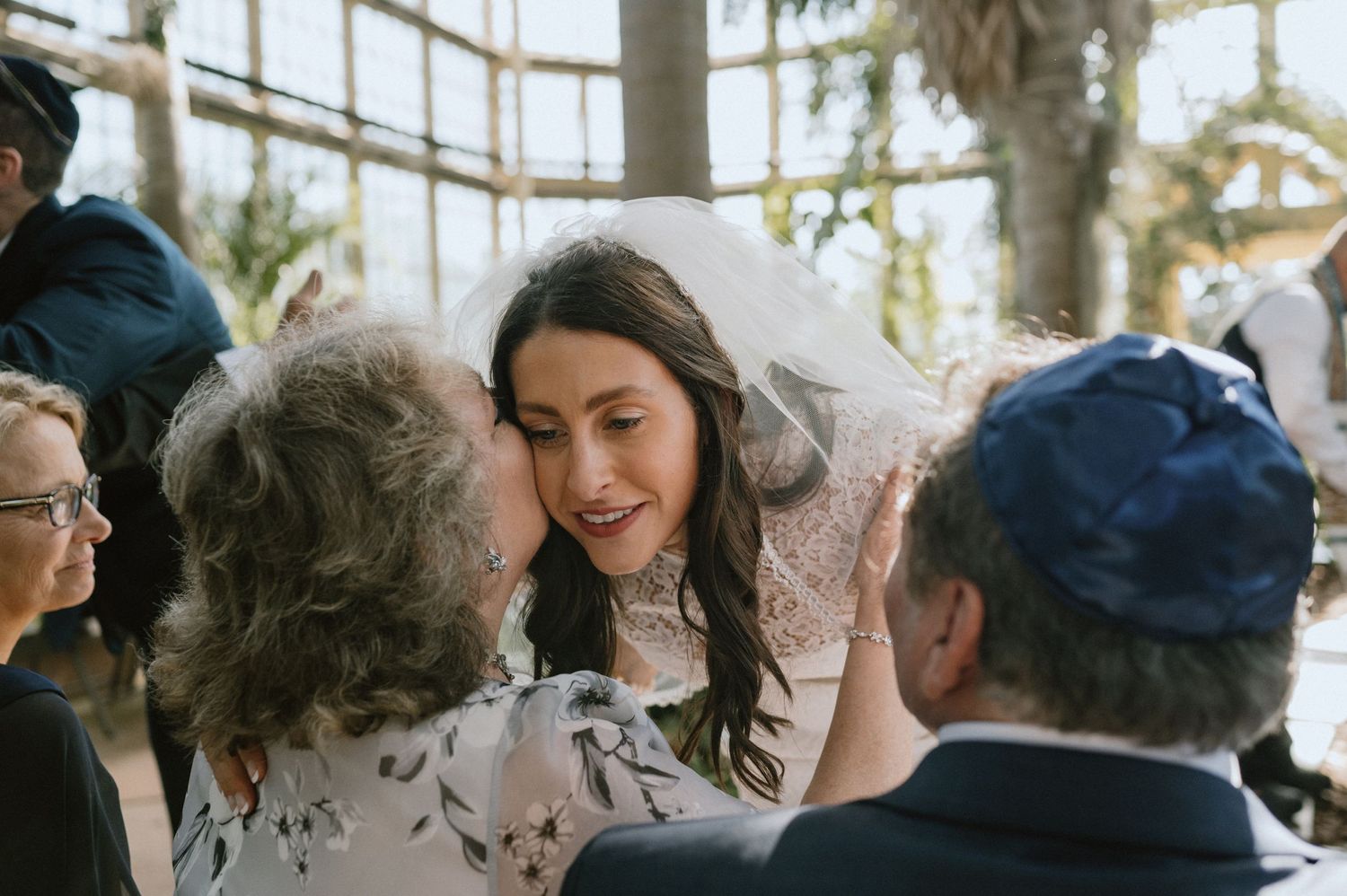 Joyful interactions between wedding guests and couple in a sunlit greenhouse.