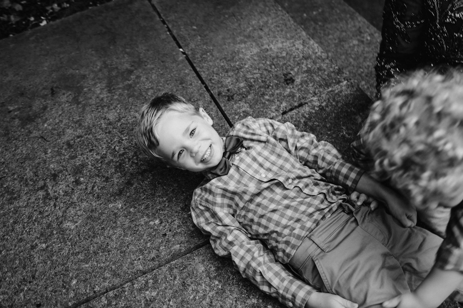 A candid black and white photo of a child lying on concrete and laughing.