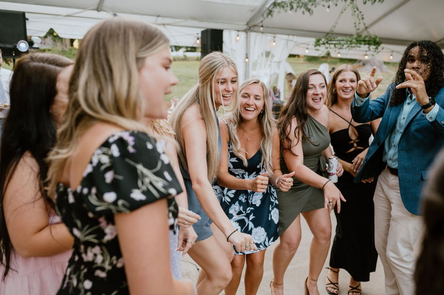Wedding guests laugh and dance together during reception under decorated tent.