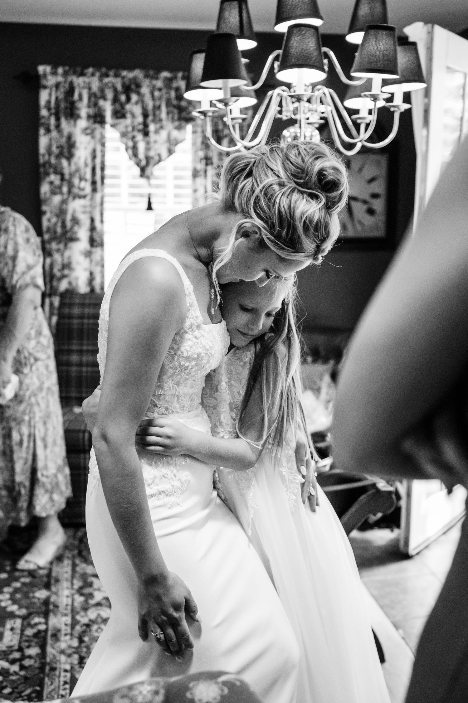 Black and white image of wedding dress preparations under an elegant chandelier.