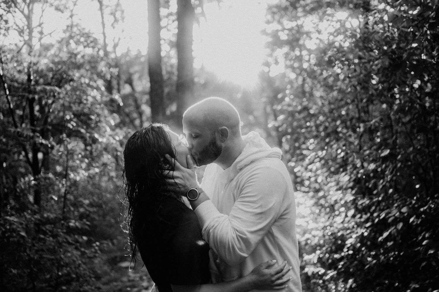 Intimate black and white portrait of couple embracing in forest setting.