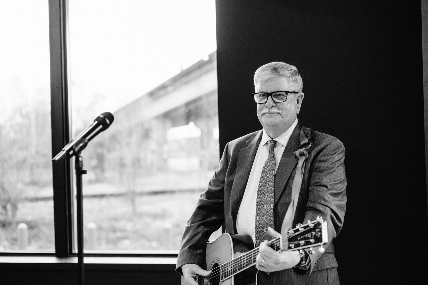 Musician playing acoustic guitar by a window in black and white photography.