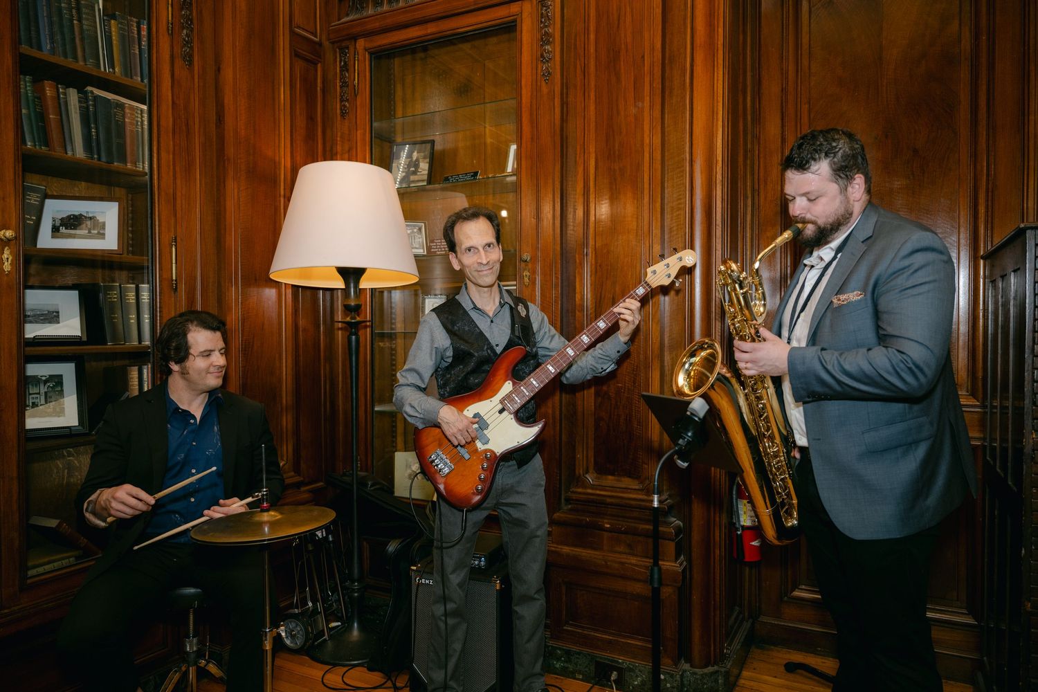 Live band performing with guitar and saxophone in a wood-paneled library setting.