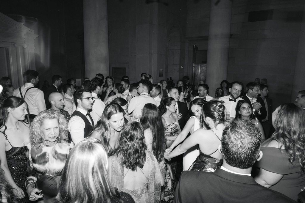 A crowded dance floor filled with people dancing and celebrating at a nighttime party or reception event.
