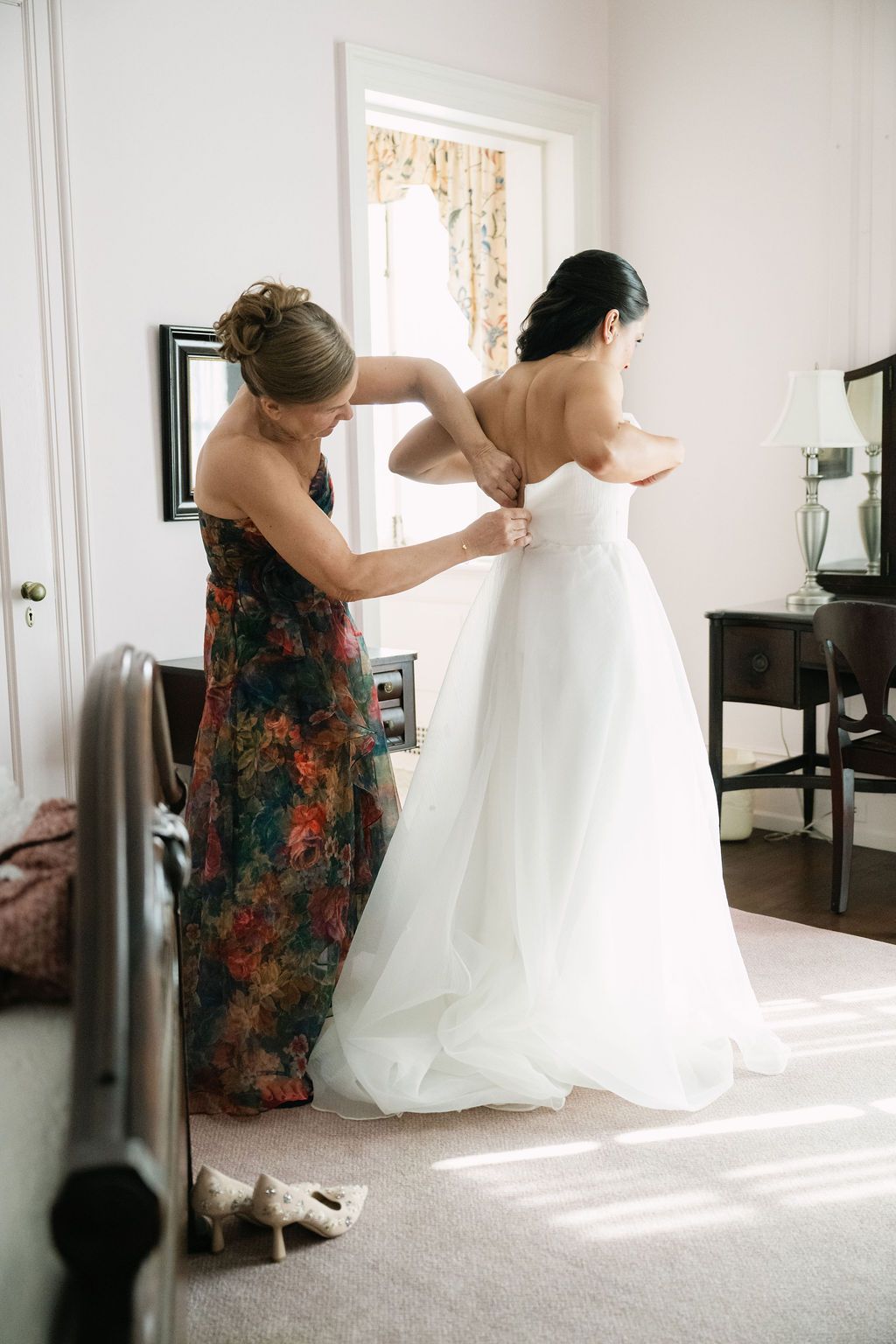 A wedding dress being adjusted and fitted in a sunlit room with floral bridesmaid dresses at Strong Mansion on Sugarloaf Mountain
