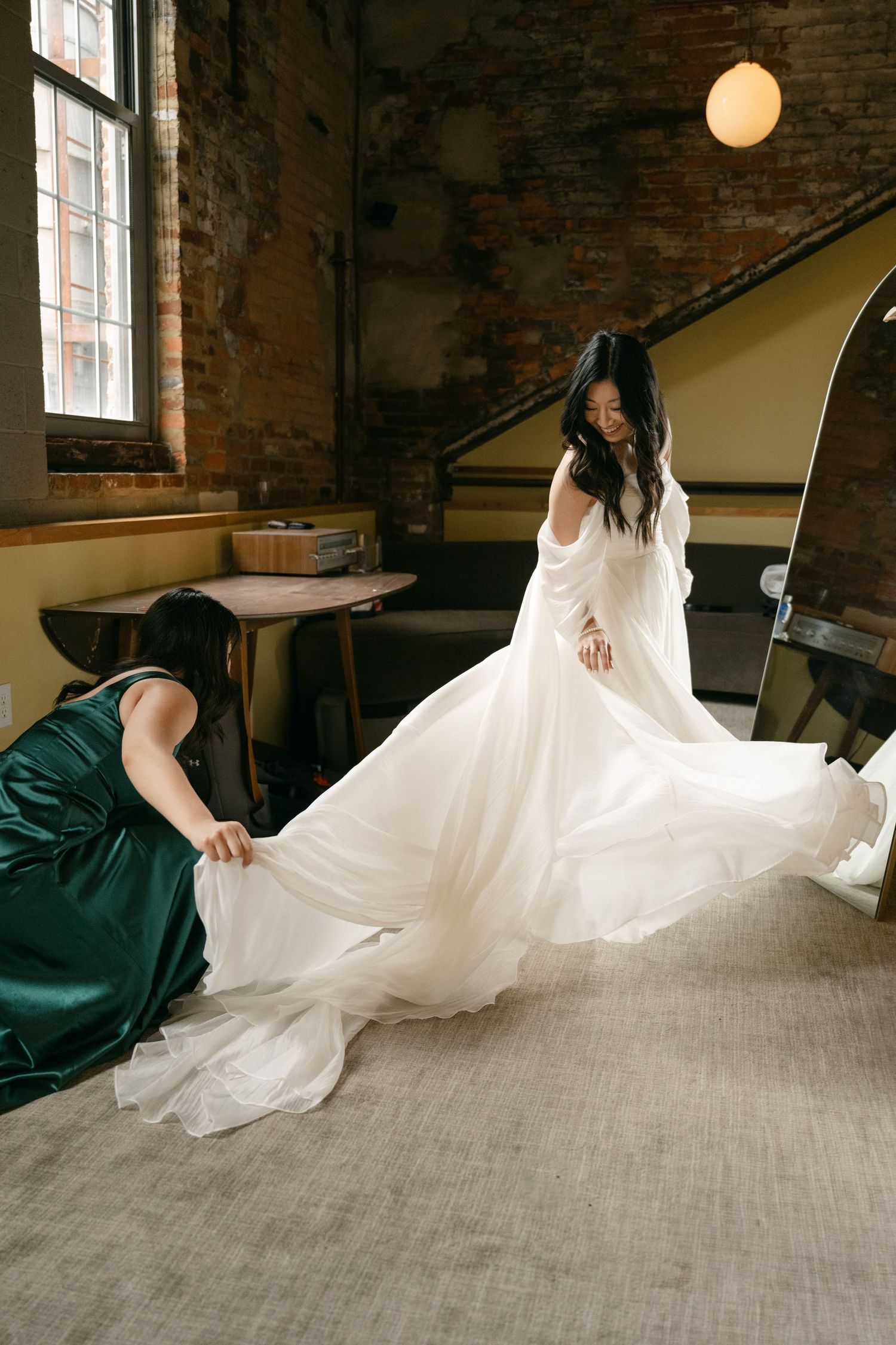Wedding dress being arranged on a grey floor in a rustic brick room.