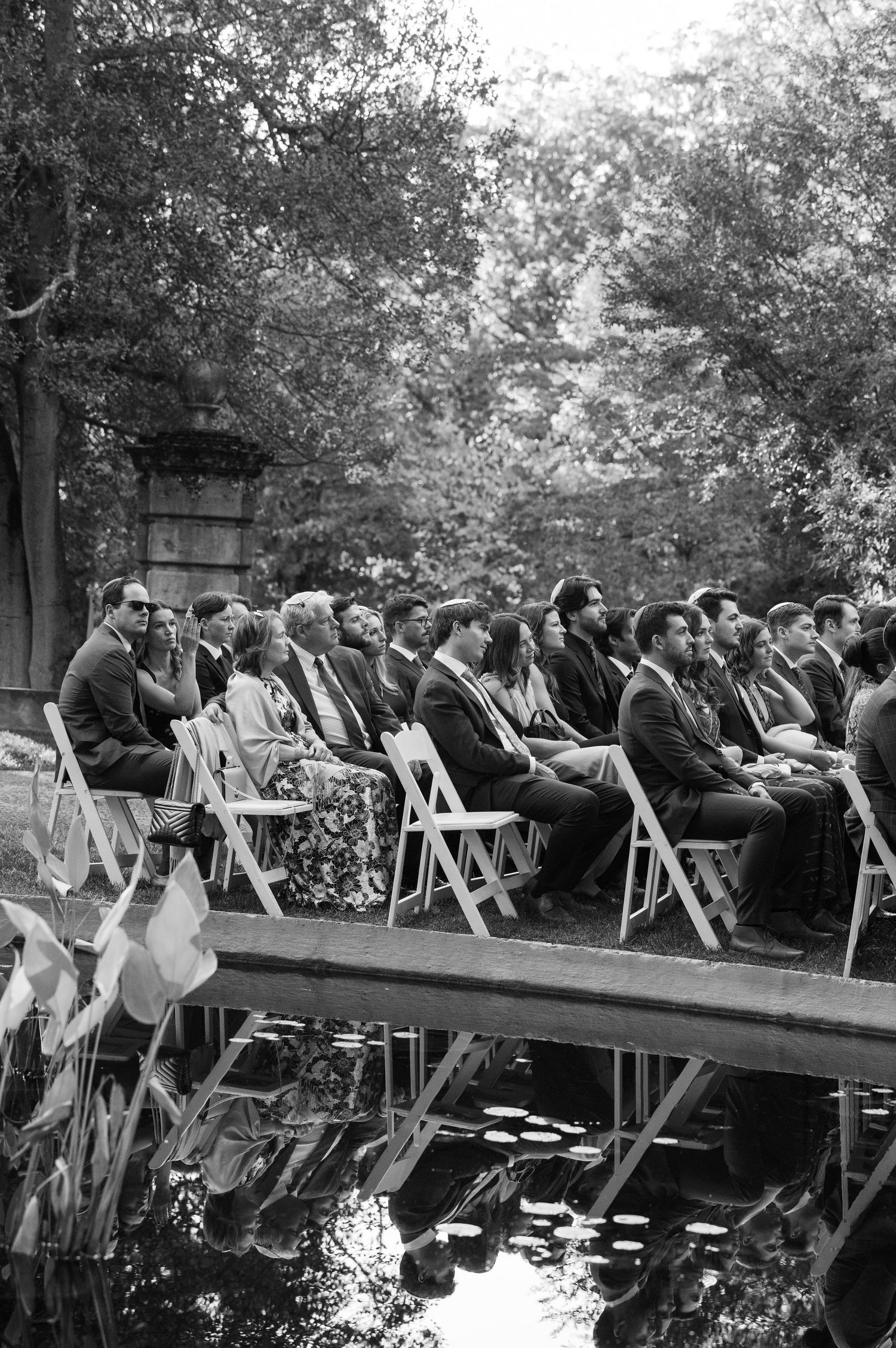 Wedding guests seated in rows of white chairs during an outdoor ceremony.