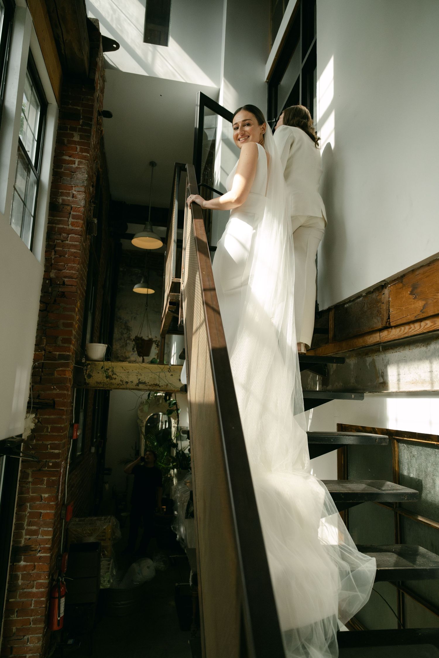 Elegant white wedding dress flowing down a rustic wooden staircase in a historic building with brick walls.