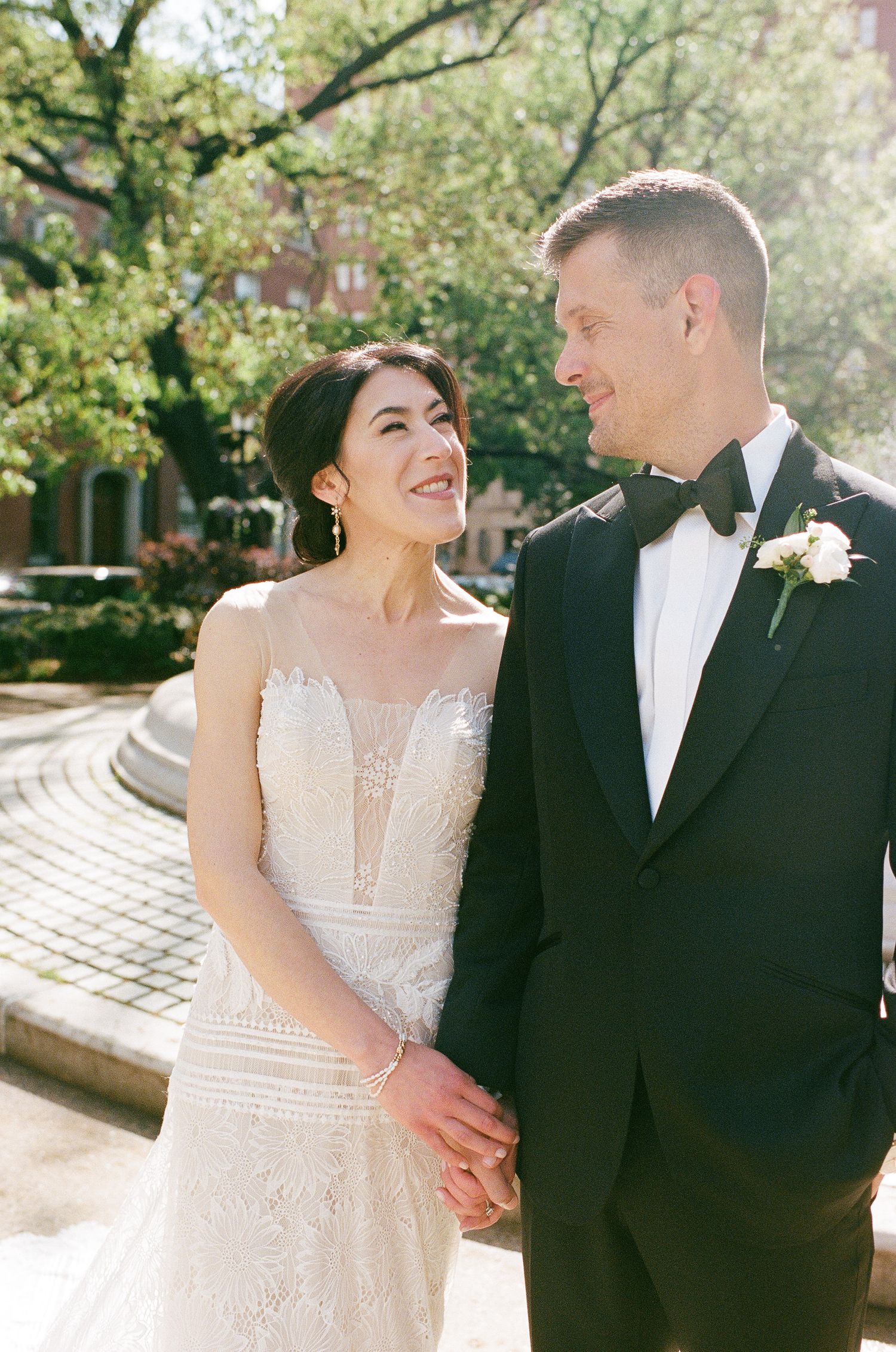 A joyful wedding moment captured in natural sunlight with greenery in the background.