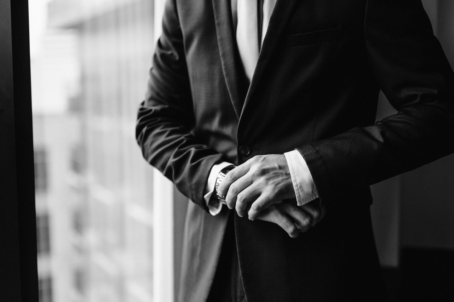 Close-up of hands in formal attire adjusting cufflinks near window.