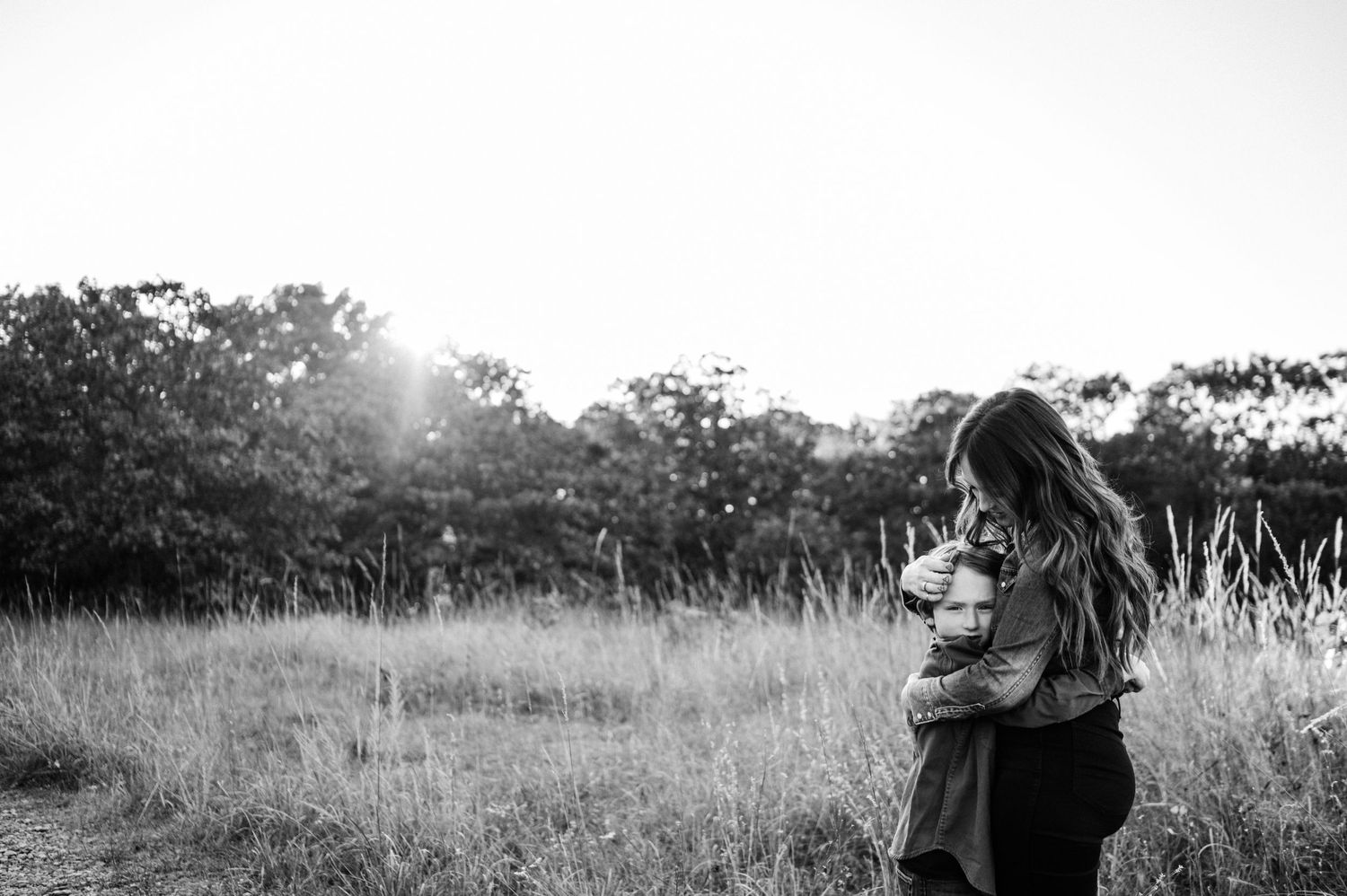 Silhouetted figures embracing in sunlit field at golden hour.