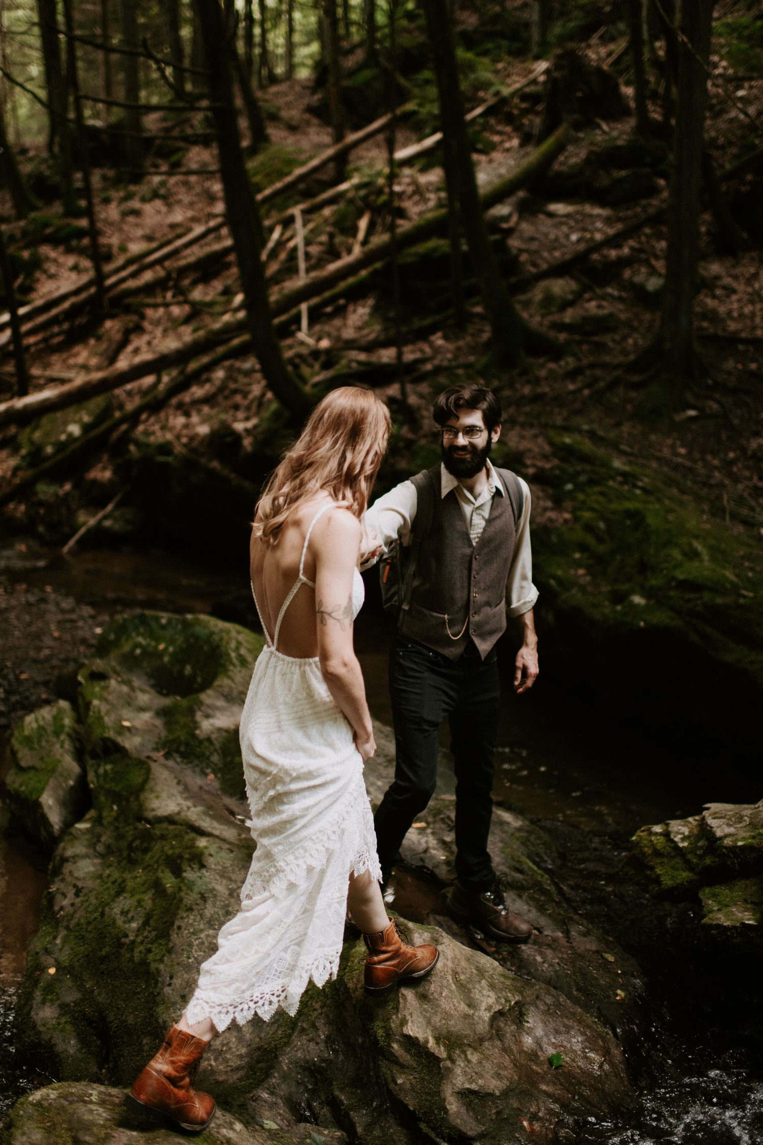A couple stands on mossy rocks in a forest setting during an intimate ceremony.