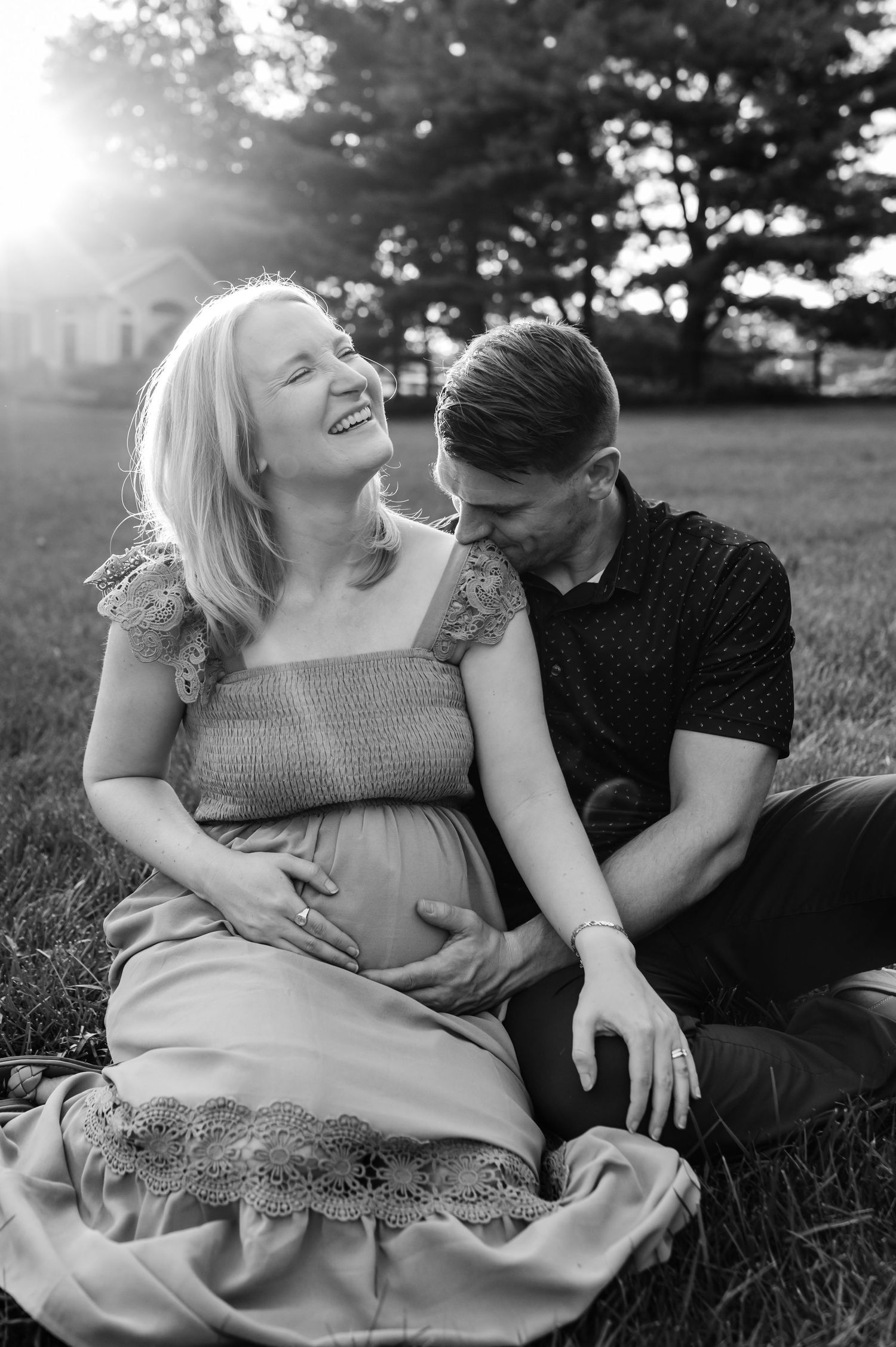 Black and white photo of couple sharing tender moment on grass at sunset.