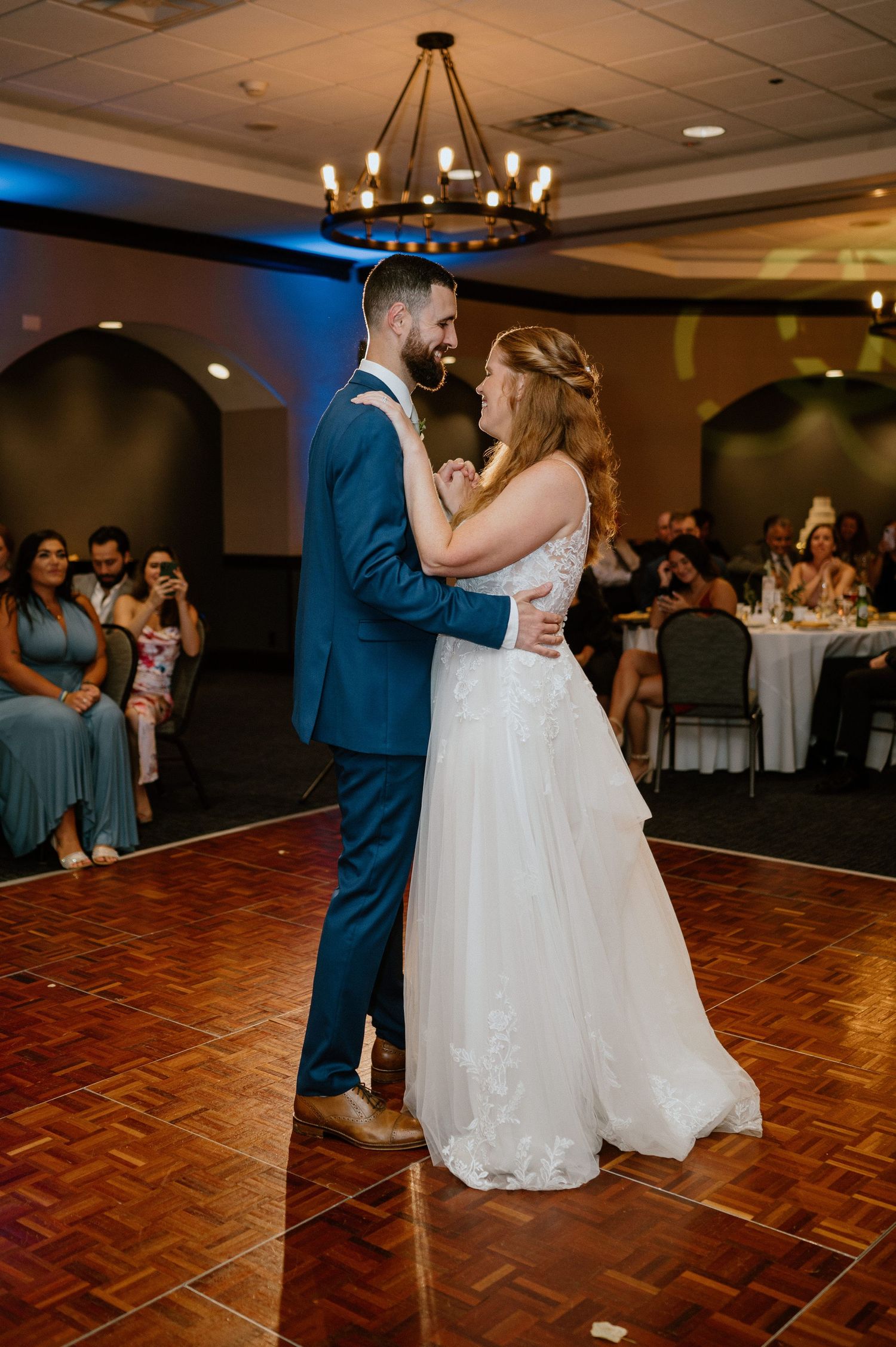 A couple shares their first dance on a parquet floor during their wedding reception.