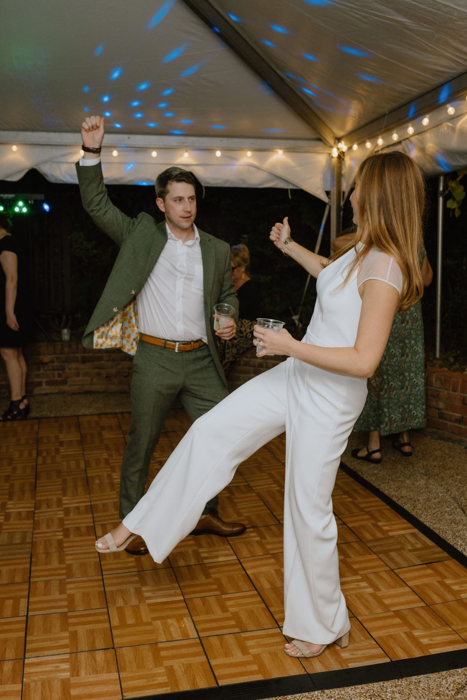 Couple dancing energetically at a party under blue disco lights and string lighting.