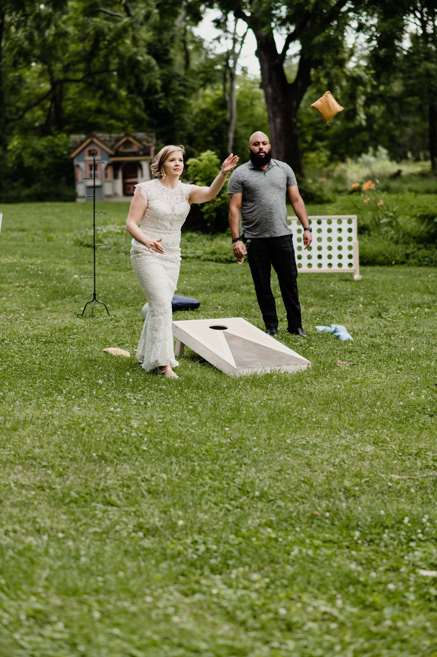 A couple playing cornhole outdoors in formal attire during a garden event.