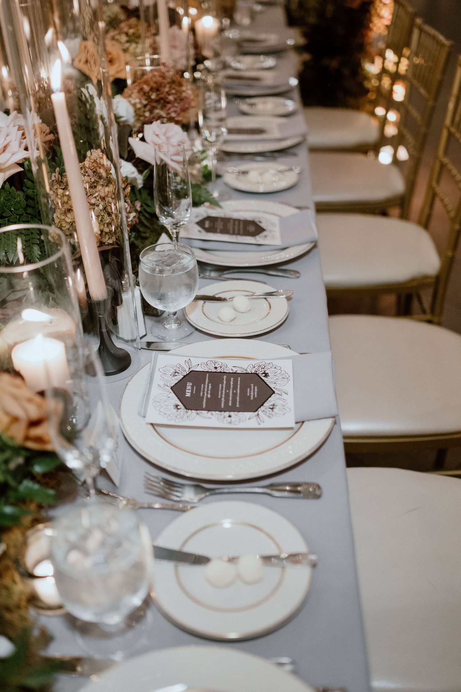 Long elegant wedding table with gold-rimmed plates, crystal glassware and beautiful floral arrangements.
