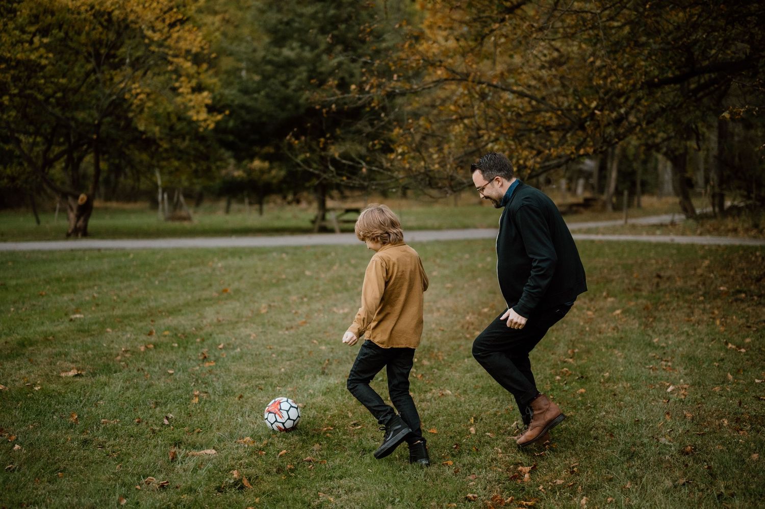 Two people playing soccer together on grass during a beautiful autumn day.