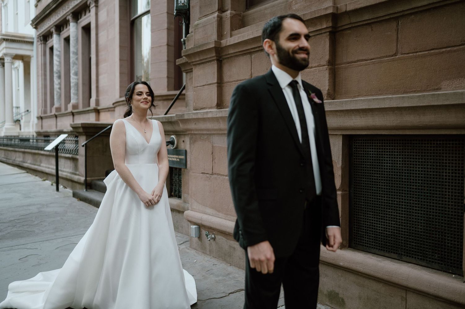 Wedding couple poses separately against brownstone building exterior.