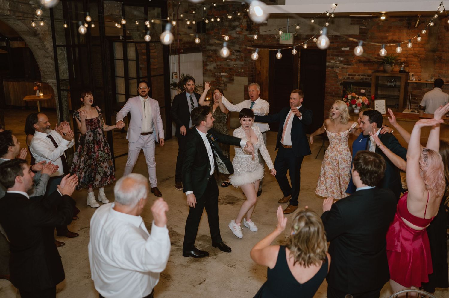 Wedding guests dancing and celebrating on a dance floor decorated with string lights.