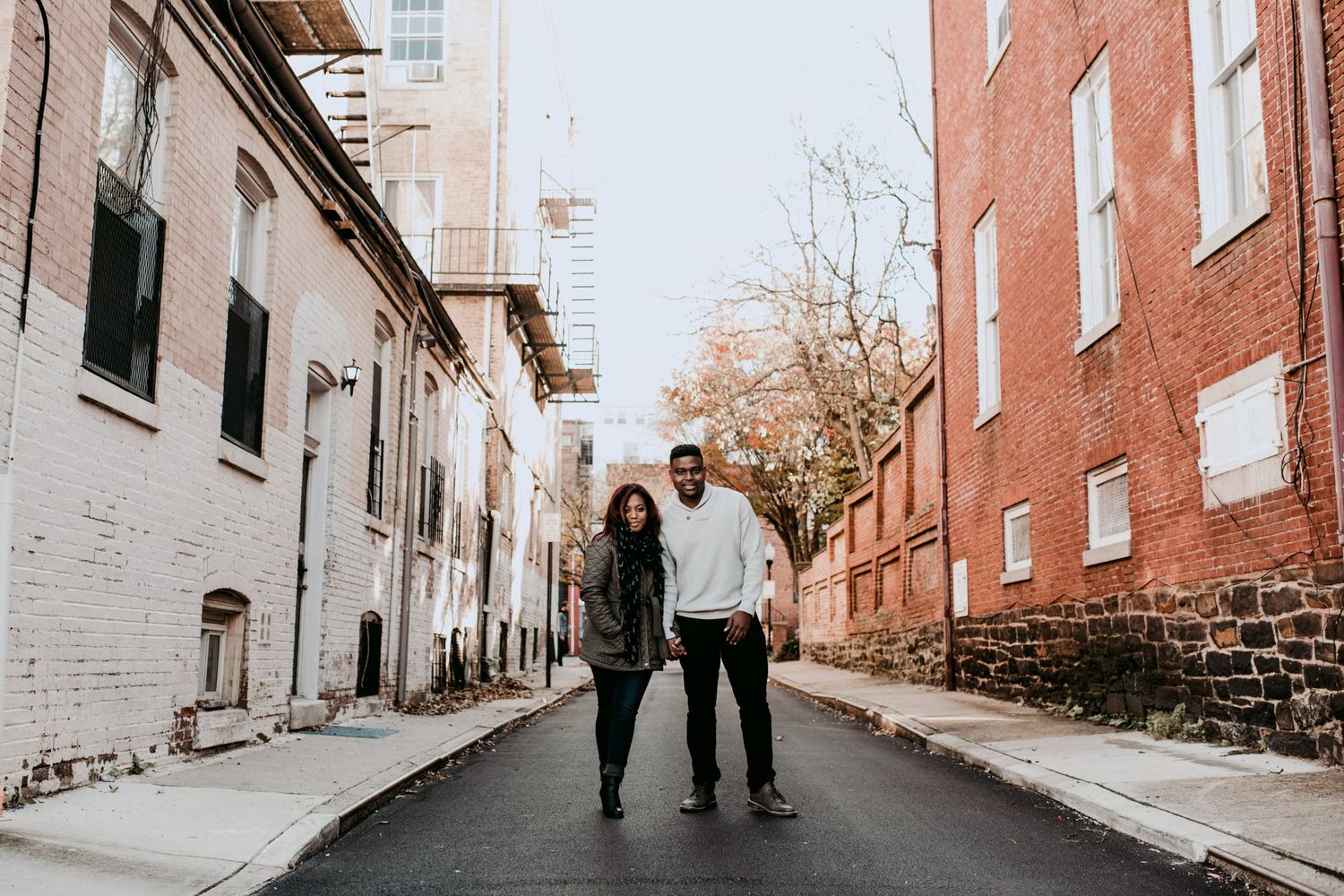 A couple walking together on a quiet city street lined with brick buildings.