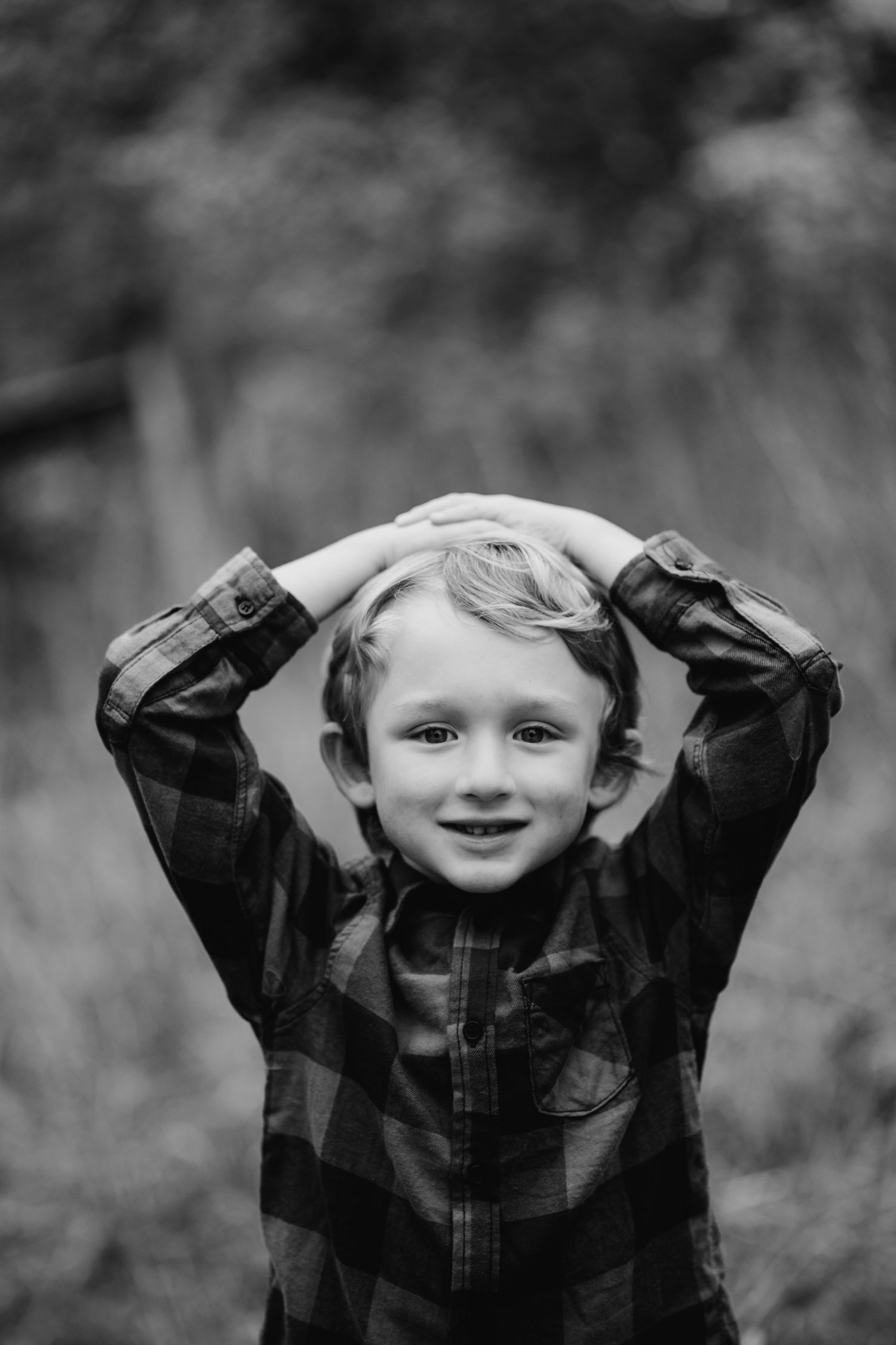 Black and white portrait of child in plaid shirt with hands on head.