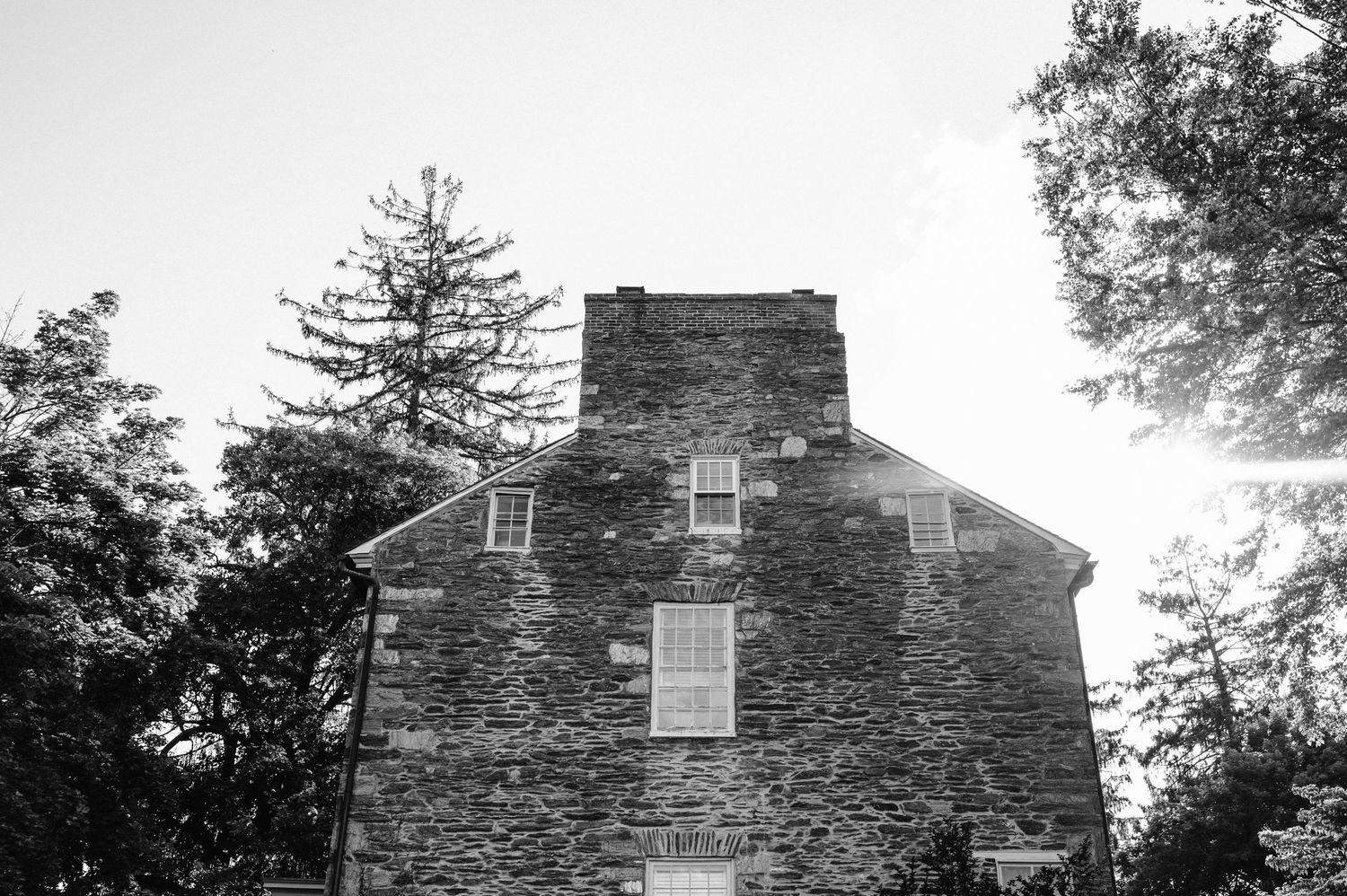 Black and white view of a historic stone house with steep roof and prominent chimney.
