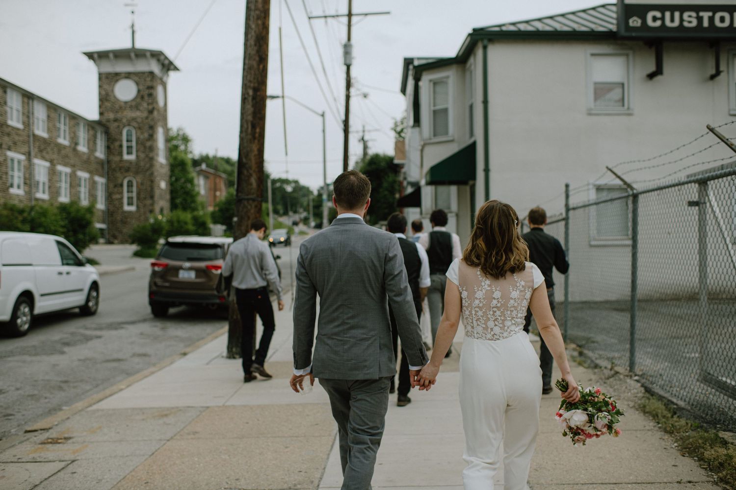 A couple walks down a city street after their wedding ceremony with a clock tower in the background.