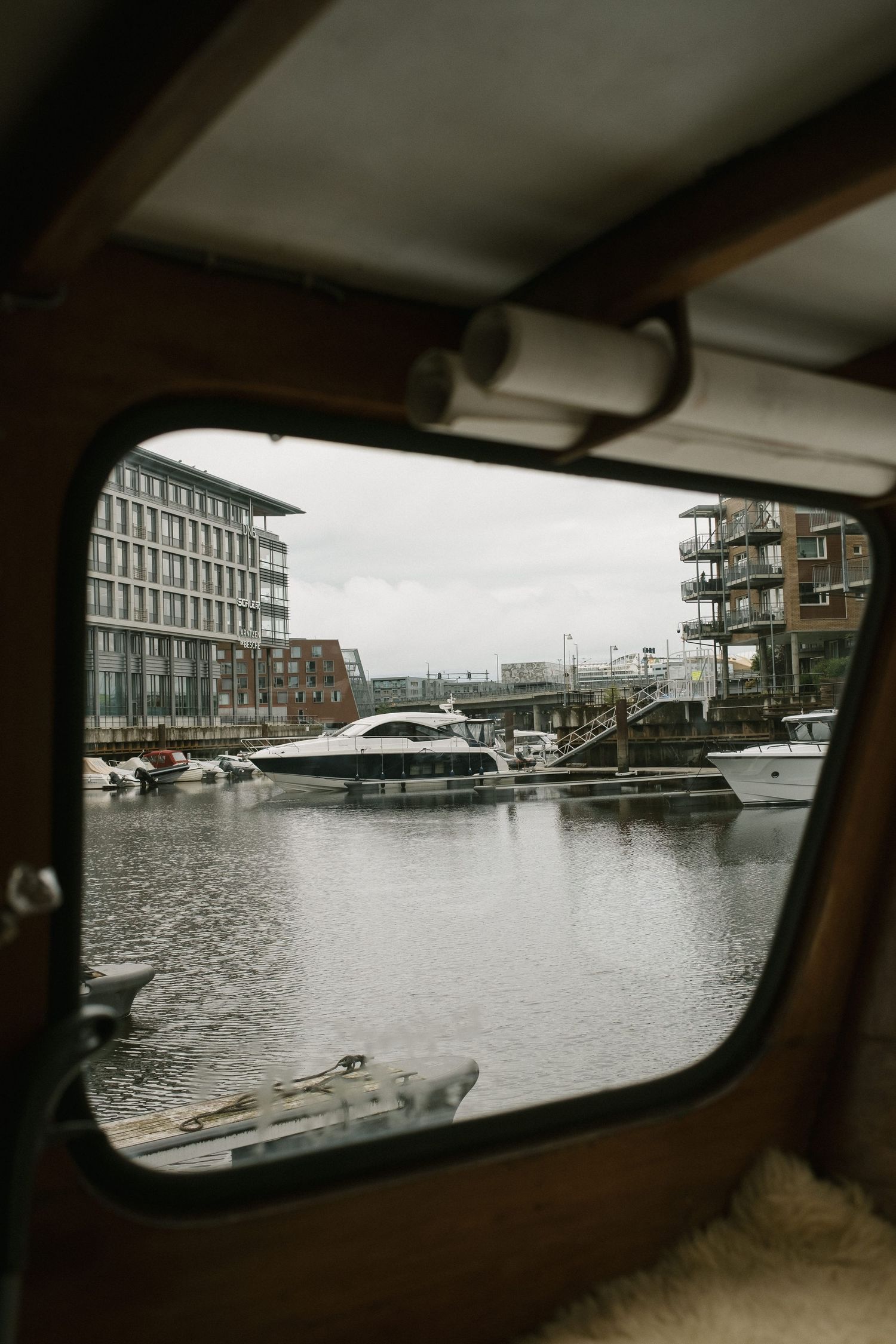 Modern marina with boats and apartments viewed through a boat window frame.