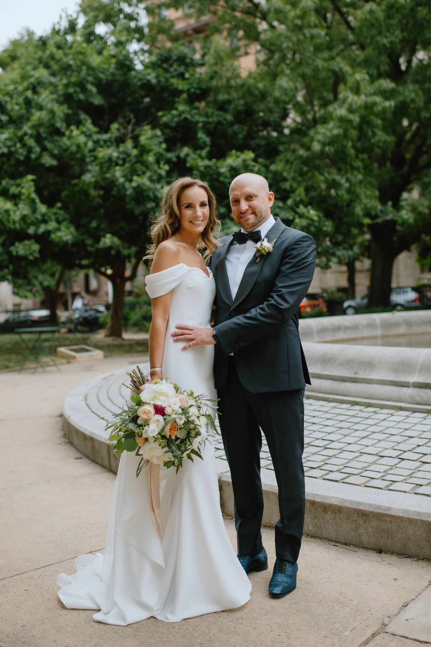 Newlyweds pose together outdoors with bride holding a beautiful floral bouquet.
