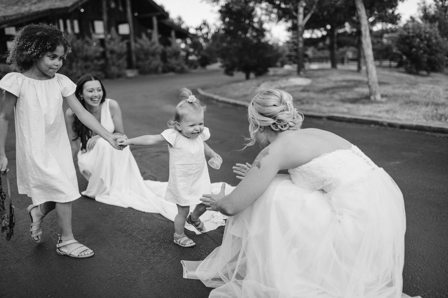 Person in a wedding dress bends down to interact with children on a residential street.