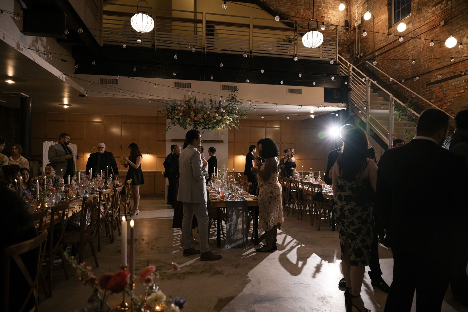 An indoor wedding reception venue with exposed brick walls, string lights, and elegantly set tables.