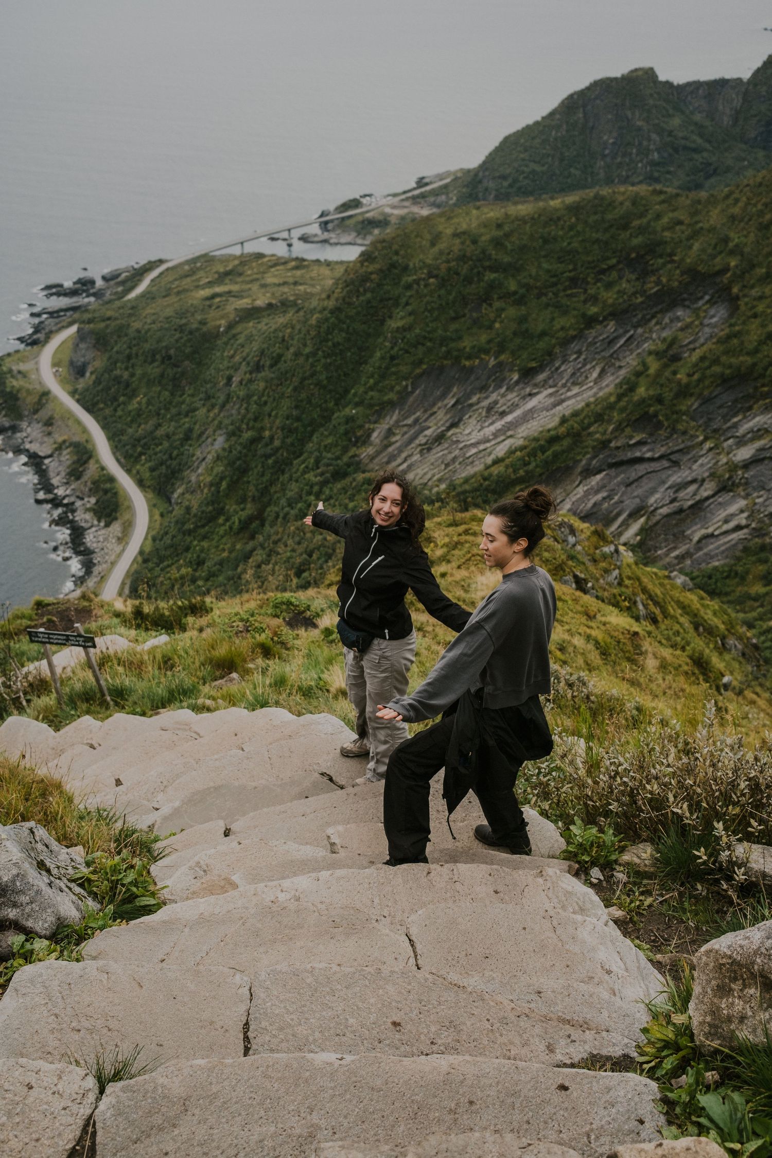 Hikers enjoying the scenic mountain trail overlooking a coastal road in Norway.