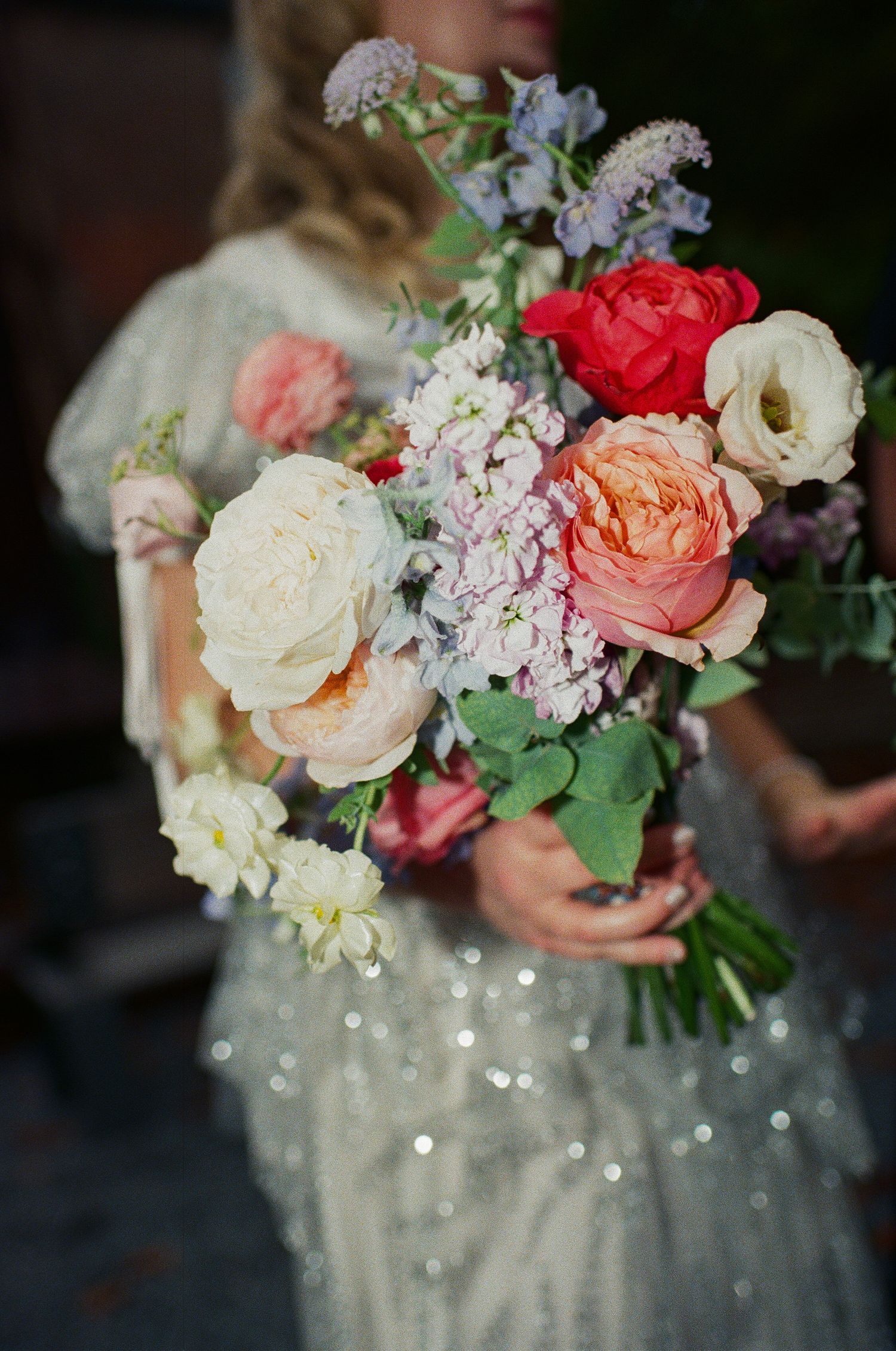 Elegant bridal bouquet features pink, red and white roses against a sparkly dress.