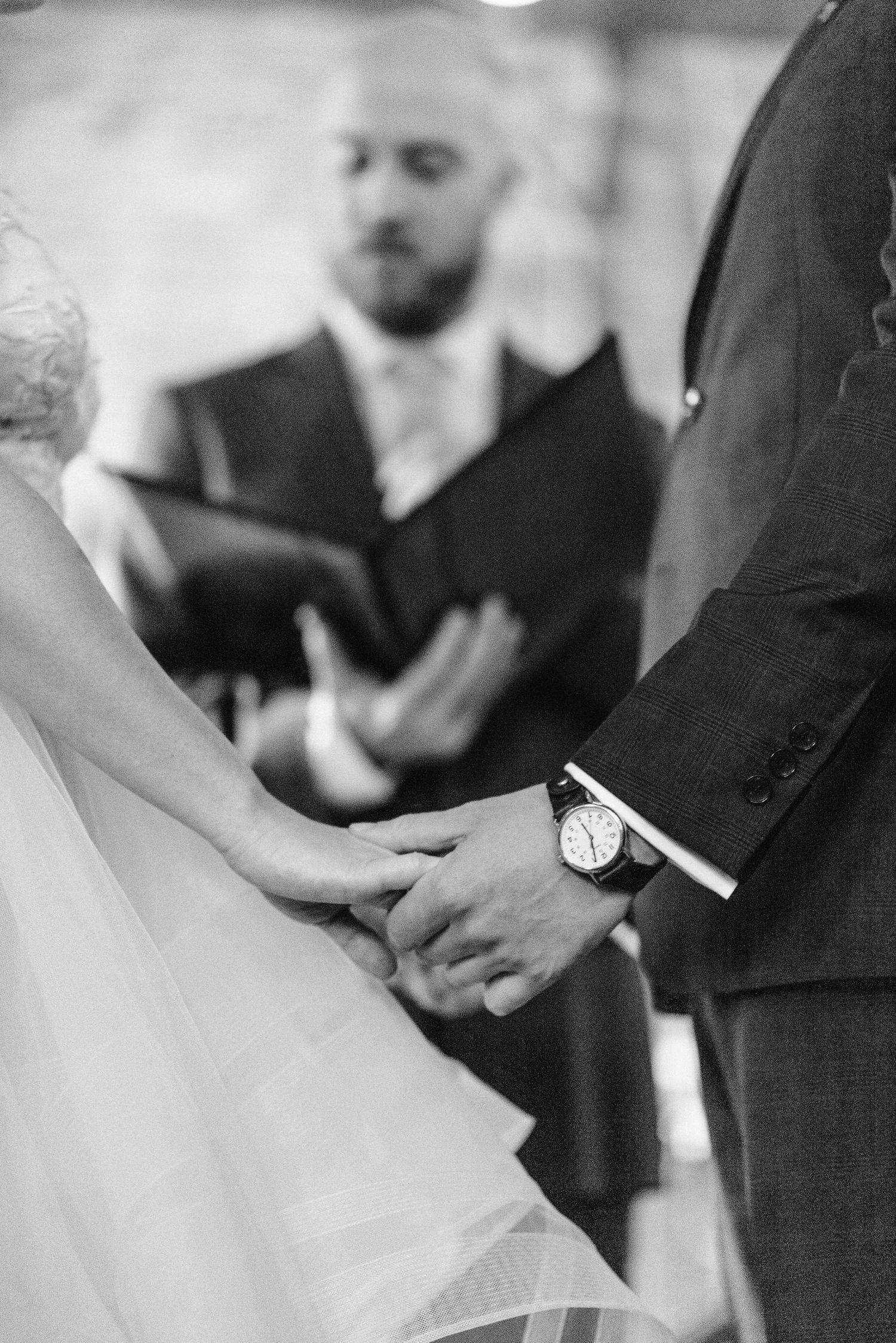 Black and white photo capturing a tender moment during ring exchange at wedding ceremony.