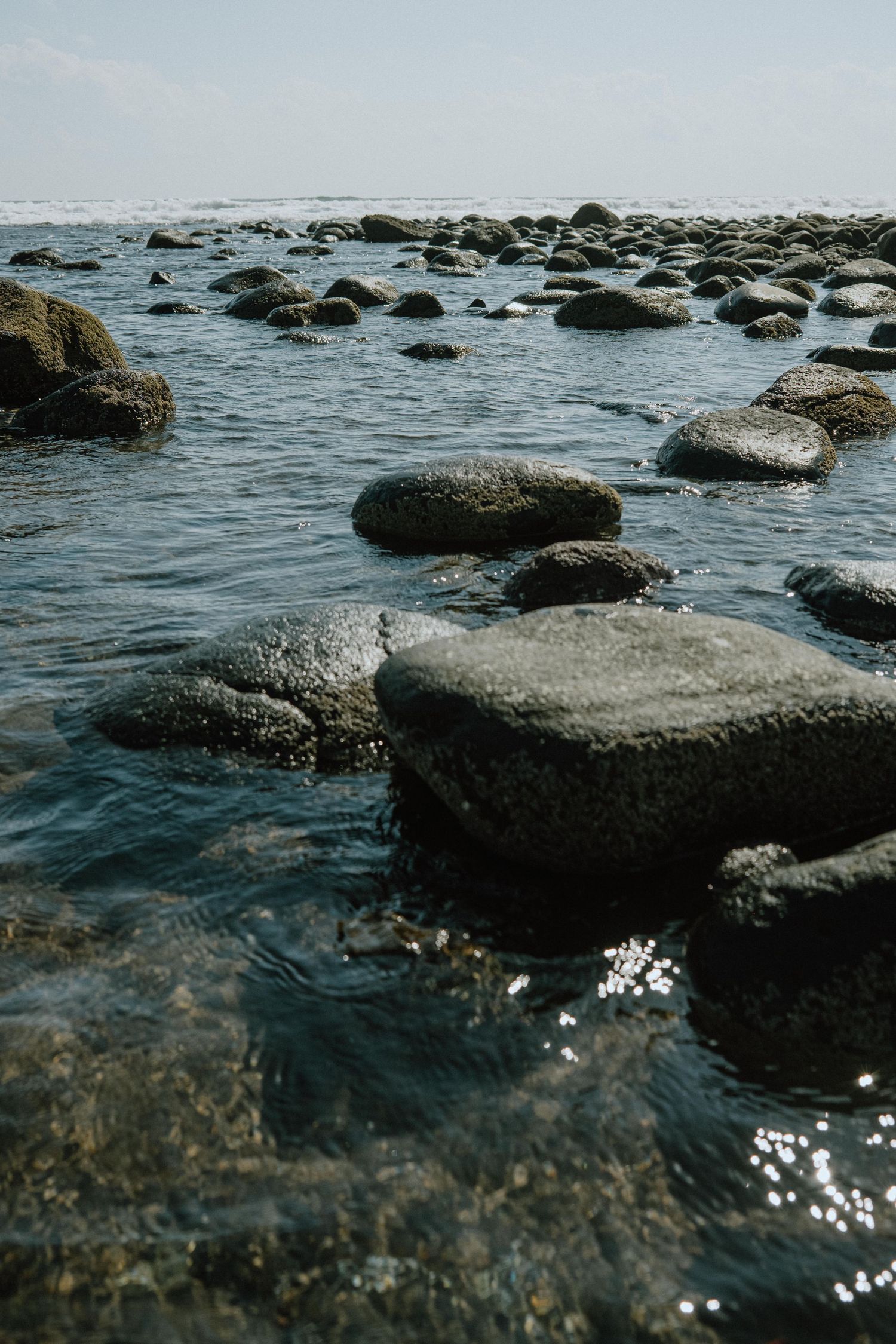 Clear blue water flowing around scattered rocks on a rocky coastline.